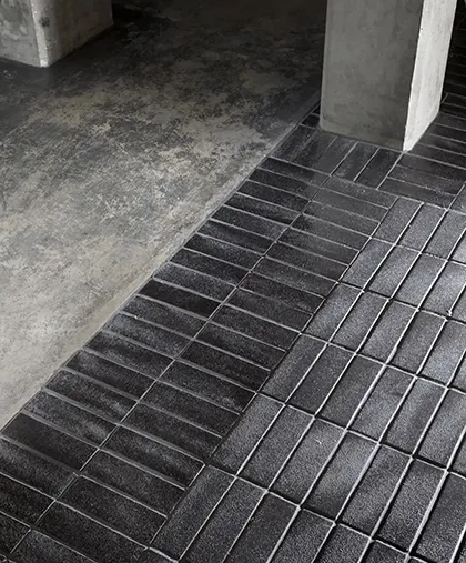 Détail d'un carrelage brique noir posé sur un sol en béton brut