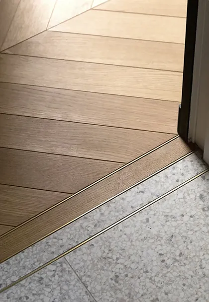 Détail d'un seuil en laiton entre parquet en chevrons et sol en terrazzo